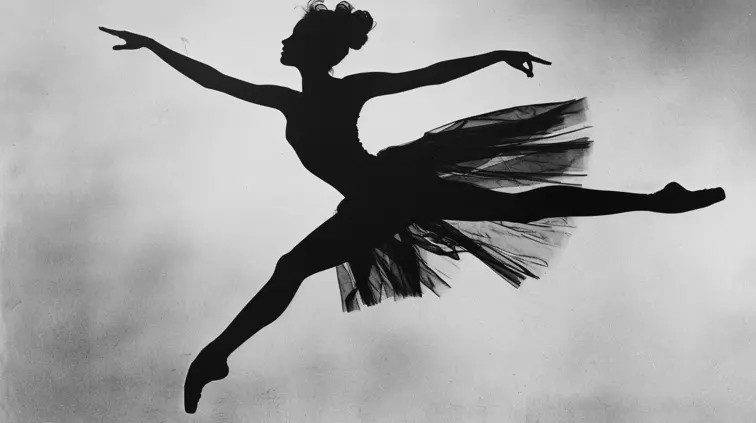 A stark, black and white portrait of a world-renowned ballerina, photograph by Richard Avedon. The dancer is caught mid-leap, her body forming a dramatic arch that stretches diagonally across the frame.