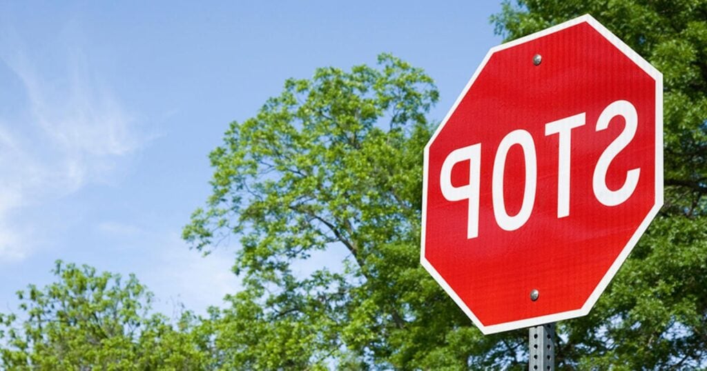 A mirrored image of a STOP sign with green trees in the background.